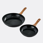 Two black frying pans with wooden handles on a light grey background